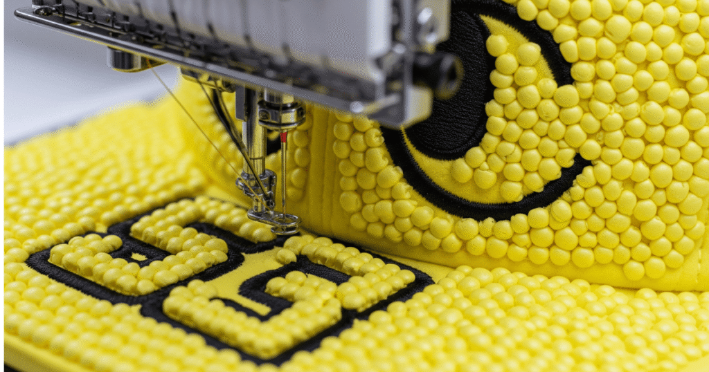 Embroidery machine running a thick satin stitch over yellow puff foam on a structured hat.